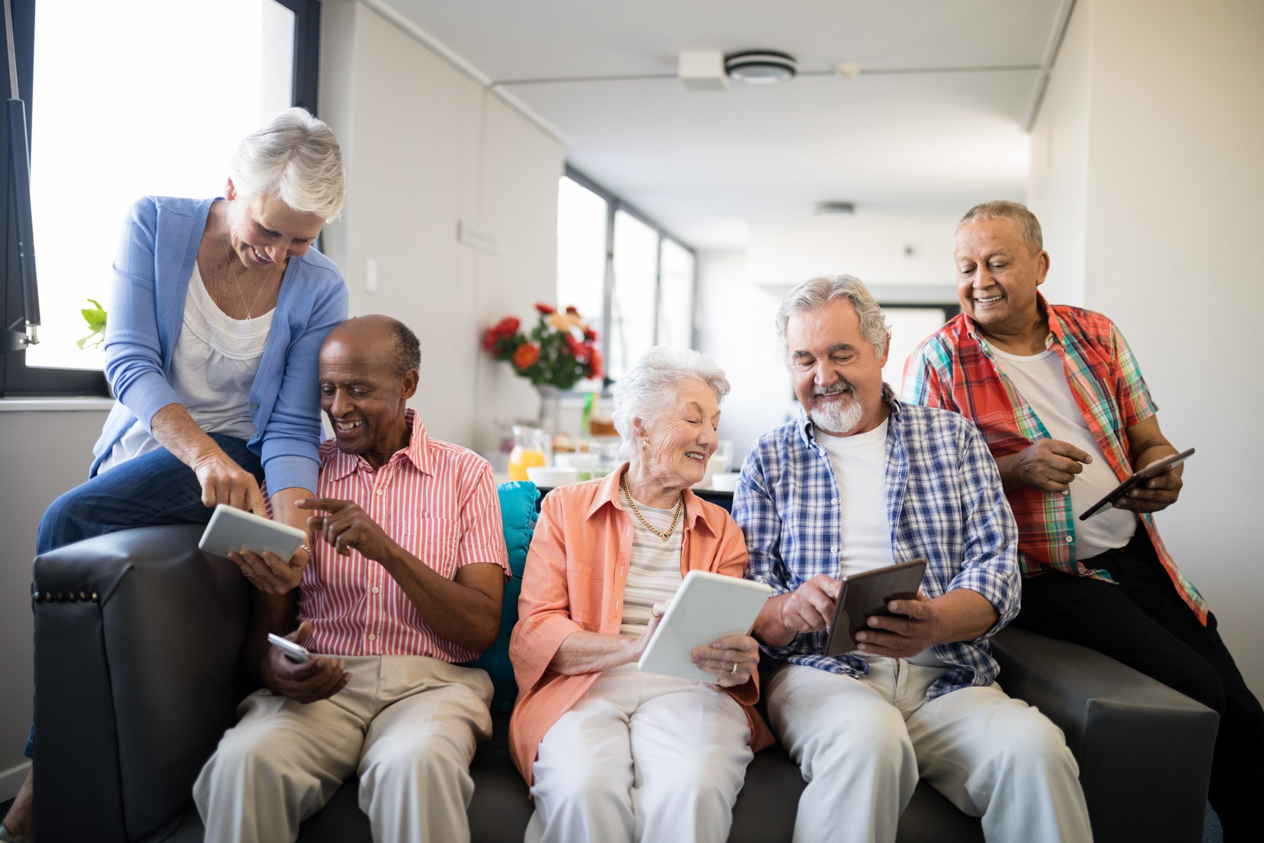 Happy senior people using tablet computers while sitting on sofa at nursing home